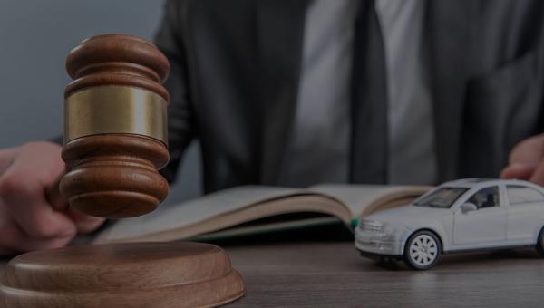 Man holding a gavel with a toy car next to it and an open book in front of him, ready to answer what happens to your car after an accident.